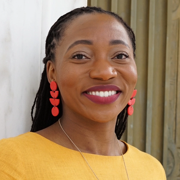 Smiling Black woman with yellow blouse and bold geometric coral colored earrings