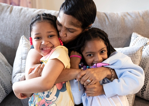 Woman hugging and kissing two smiling young children sitting on a couch.